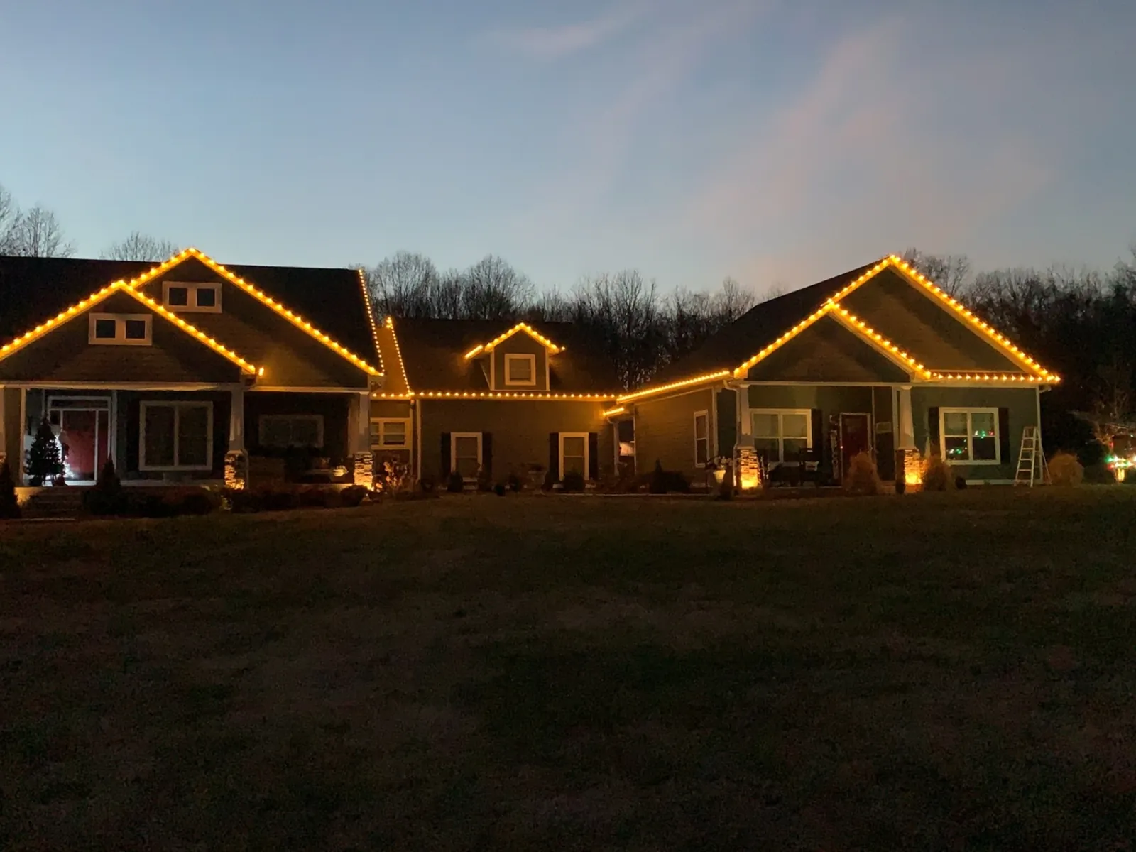 A long single story home with warm white lights following every gable and eave against a dusk sky