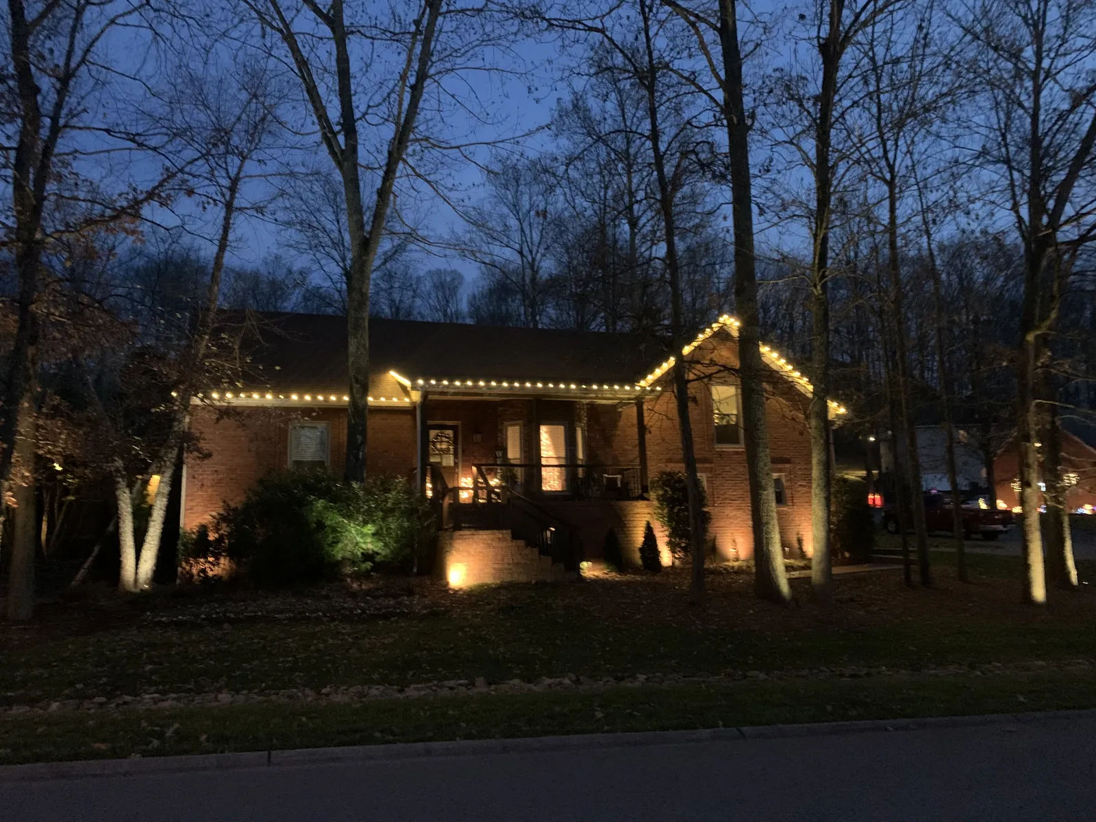 A low brick ranch under bare trees, warm white along the roofline and light rising from the flower beds